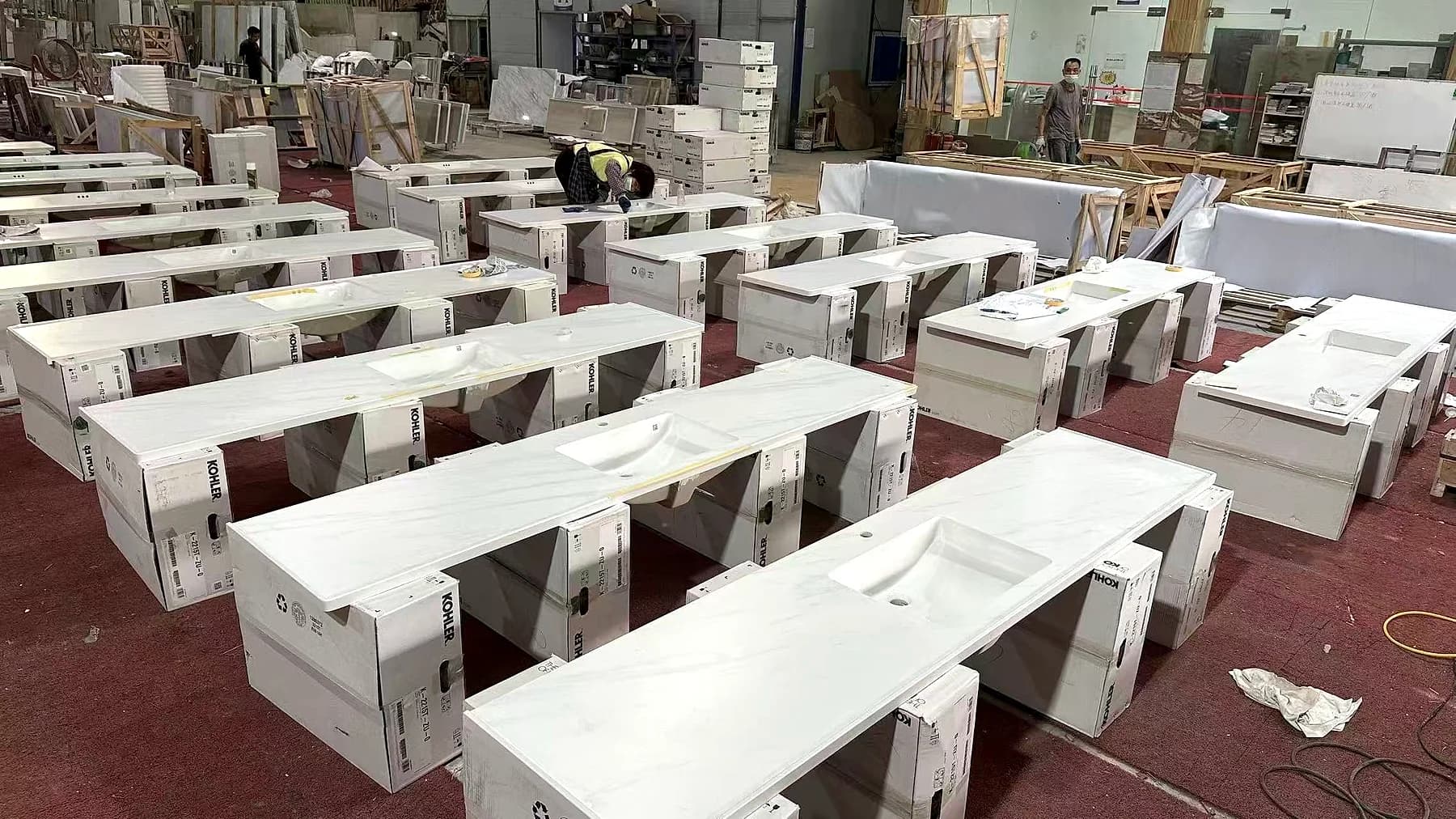 Rows of light stone vanity components with rectangular basin openings in a workshop.