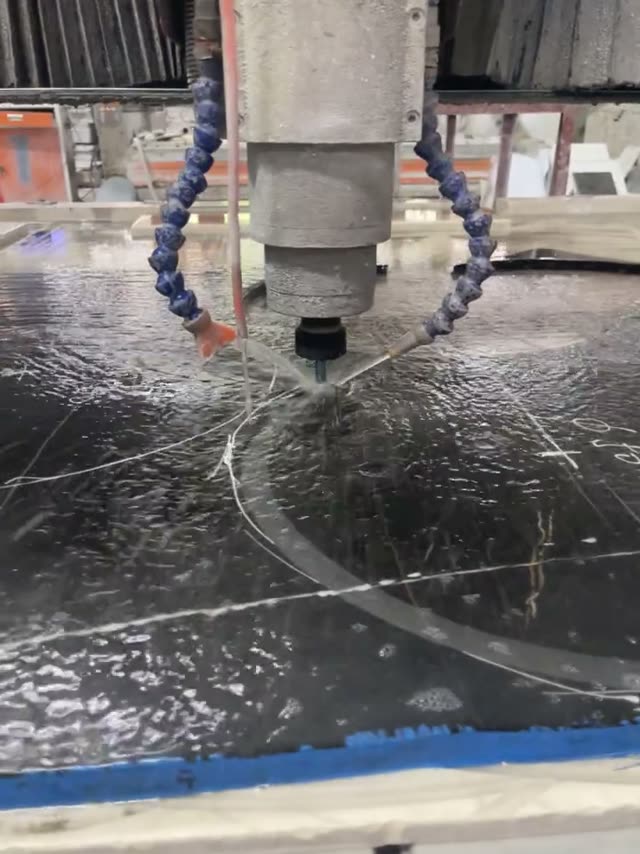 A cutting head moves across a dark stone workpiece; the machine model is not identified.
